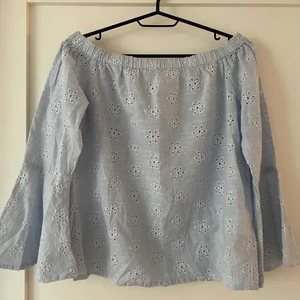 Ljusblå blus - Ljusblå off shoulder blus i strl 36/S med vita broderade blommor, (innanför broderiet är det ihåligt). Blusen är i skjortmaterial (och 100% bomull)💙 Ärmarna är utsvängda i en volang från armbågen💙 Blusen är köpt på Only och är i gott skick