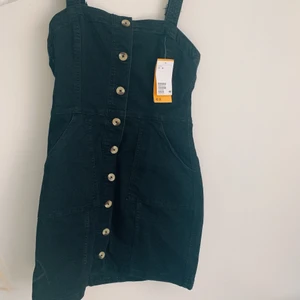 Svart jeansklänning, NY, H&M - Helt ny med prislapp kvar. Svart jeansklänning. Storlek 38. Reglerbara axelband. Knappar i fram. 