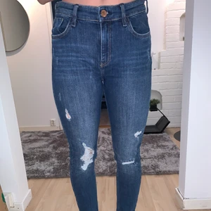 Jeans med slitningar från River island - Ett par snygga jeans med slitningar ifrån River Island. Är som nya då jag bara andvänt dom ett fåtal gånger. Snygg mörkblå färg. Storlek 12/38/40/M skulle säga att dom passar en M.