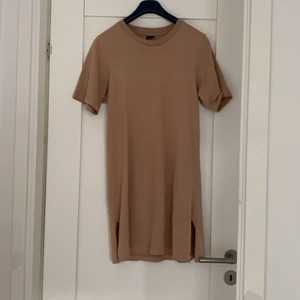 Beige T-shirt klänning - En mörkare beige T-shirt klänning från Gina Tricot, stl S. Den har två slits på sidorna men är ändå inte för kort. Säljer då den inte kommer til använding längre. Skriv i chatten för bild på, möts inte upp och köparen står för frakt.