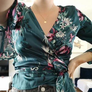 Blommig blus från GinaTricot i storlek 38 - Mörkgrön blommig blus från GinaTricot i storlek 38 i omlottmodell och trekvartsärm. Jag på bilden är 170 cm lång och har vanligtvis 36/S i blusar.