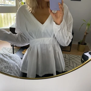 Vit blus i peplum-modell från NA-KD - Vit blus i bomullstyg från NA-KD. Charmig peplum-modell (går inåt vid midjan och sedan svänger ut vid höften). Dragkedja i sidan. Storlek 42. Gott skick.