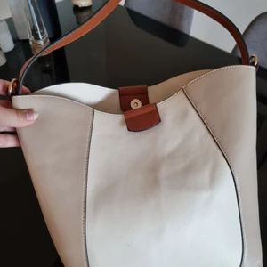 Beige och brun handväska  - Smart fack i mitten så att du lätt hittar dina saker. Detta facket är också uttagbart. Guldbeslag och det följer med ett längre justerbart beiget axelband med guldbeslag.