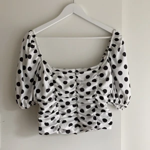Prickig blus från ASOS Design  - Vit blus med svarta prickar. Resorband så den sitter på axlarna, kan även användas hängandes längs axeln. Aldrig använd. Säljer pga överskattade min egen stil, dock så fin och önskar den klädde mig. 