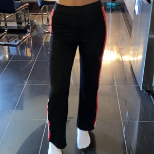 Lösa svarta byxor size S - Bekväma lösa svarta byxor med röda och vita linjer vid sidorna. Sitter tajt vid höfterna men blir lösare vid benen. Högmidjad och bekväm. Oanvända endast testade och i bra skick. Det är storlek S men kan töjas ut mycket då tyget är väldigt elastiskt.