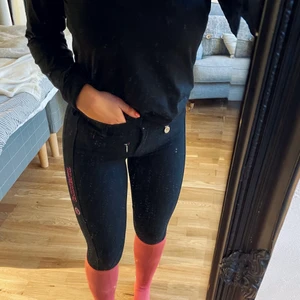 Pikeur Ridbyxor  - Halvskodda ridbyxor från Pikeur i storlek 164. Svarta med cerise logga på vänstra låret. Det rosa på vaderna är strumpor!