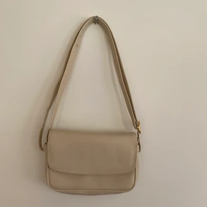 Handväska  - Beige handväska med guldiga detaljer. Kan göra bandet till både crossbody eller att ha över axeln. Köpt secondhand men ser i princip oanvänd ut. 