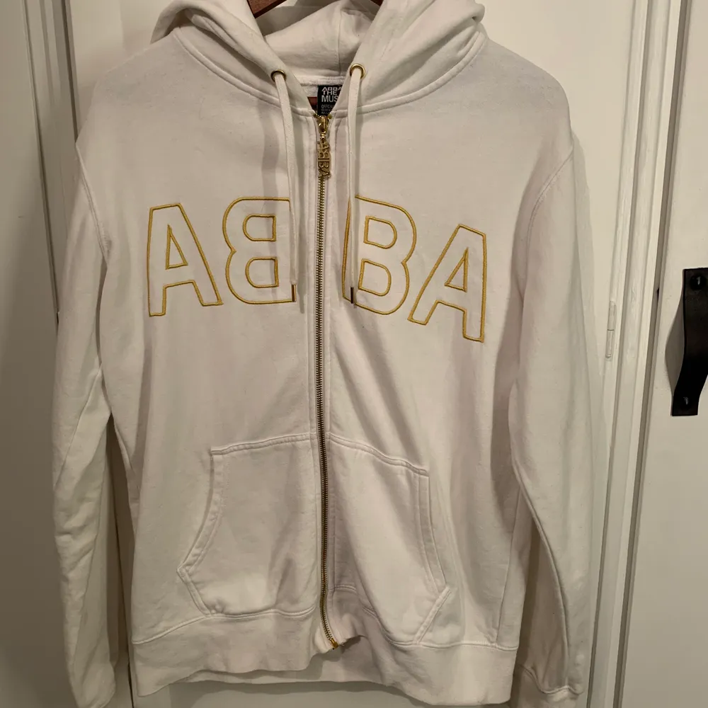 En vit zip up hoodie/ kofta med guld detaljer som är köpt från ABBA museet. Har inte haft användning av den på ett tag och den är i ett fint skick men dock med ett fåtal fläckar som enkelt kan tas bort.. Tröjor & Koftor.