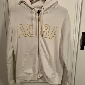 En vit zip up hoodie/ kofta med guld detaljer som är köpt från ABBA museet. Har inte haft användning av den på ett tag och den är i ett fint skick men dock med ett fåtal fläckar som enkelt kan tas bort.