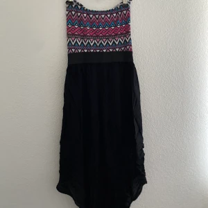 Klänning  - Axelbandslös klänning med fjäder för att framhäva midjan.  Baksidan är längre.