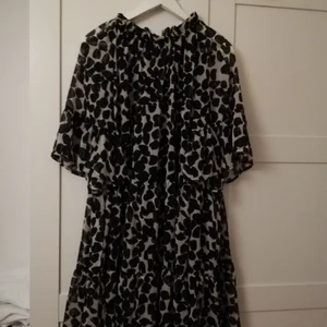 Klänning - Luftig och lös klänning med svarta fläckar på benvit bakgrund. Har knytning i nacken. Jag har haft den på mig 2 ggr med svart skärp. 