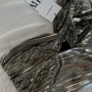 Silvrig festtopp  - Superfin festtopp med ett band på ena sidan. Dragkedja på sidan för att kunna ta på lätt. Är lite stor på mig och därför säljer jag den, helt oanvänd och har fortfarande prislappen kvar. Storlek S men passar även en M beroende på hur stor byst man har. 