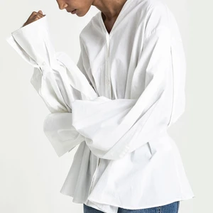 Dagmar | Penny Blouse - Penny Blouse i ekologisk bomull från Dagmar. Aldrig använd. NWT. Sydda motveck fram i midjan och infälld resår mitt bak. Extra lång, vid ärm med lagda veck nertill och bred manschett. V-ringad hals och knappslå hela vägen fram. 