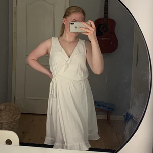 Vit klänning - Vit klänning från Vero Moda perfekt till student och skolavslutning! Volang nertill och i urringningen med en knytning i median. Som ny använd endast en gång. Köparen står för frakt.