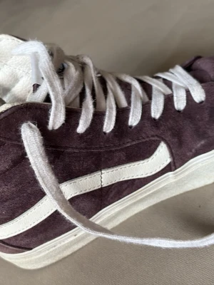 Lila Vans Sk8-Hi sneakers mocka - Säljer ett par klassiska Vans Sk8-Hi sneakers i lila mocka med vit sula och vit sidostripes. Skorna har snörning och hög modell som ger en retro vibe. Perfekta för dig som vill ha en stilren och tidlös sneaker med skön passform.