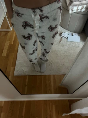 Fluffiga vita loungewear-byxor - Supermysiga vita loungewear-byxor från Censored med brunt och rött mönster. Byxorna har en fluffig, mjuk känsla och dragsko i midjan för bästa passform. Perfekta för chill hemma eller mysiga kvällar. Materialet är polyester.