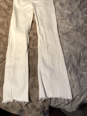 Vita bootcut jeans med rå kant - Säljer ett par vita bootcut jeans med rå, fransig kant nedtill. Jeansen har en klassisk femficksmodell och är tillverkade i ett mjukt bomullsmaterial. Perfekta för dig som gillar en avslappnad men trendig look. 