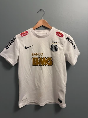 Vit Santos Neymar Jr matchtröja - Säljer en vit Santos matchtröja från Nike med Neymar Jr och nummer 11 på ryggen. Tröjan har flera sponsorer tryckta i svart, guld och rött samt klubbmärke på bröstet. Tillverkad i lätt och ventilerande material, perfekt för fotboll eller träning. Är från fotbollsmarknaden