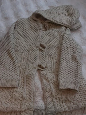 Beige stickad hoodie från Zara - Stickad hoodie från Zara i beige med grovstickat mönster och snygga träknappar. Tröjan har huva och detaljerade flätstickningar längs fram och ärmar. Perfekt för dig som gillar mysiga och stilrena plagg i mjukt material.