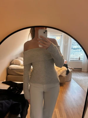 Grå off shoulder stickad tröja - Snygg grå stickad tröja med off shoulder-modell och långa ärmar. Tröjan har en bred krage som vilar över axlarna och är figurnära i modellen. Perfekt för dig som gillar en trendig och stilren look.