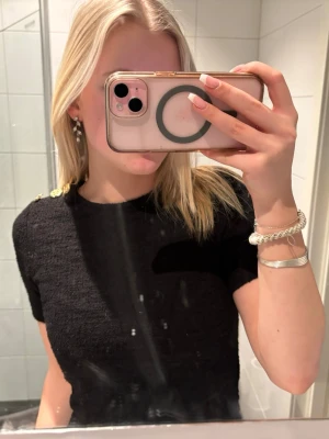 Svart topp med guldknappar - Snygg svart topp med korta ärmar och tre guldknappar på axeln. Tjockare, strukturerat material! Helt ny och aldrig använd med prislappen kvar ❣️