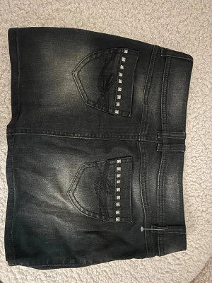 Svart lågmidjad jeanskjol med nitar  - Cool svart lågmidjad jeanskjol med slitna detaljer och silvriga nitar på fickorna. Passar 32/34. Köpt second-hand men är från EDC💞