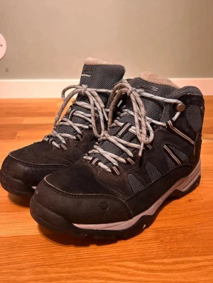 Svarta kängor med snörning Hi tec - Säljer ett par svarta sneakers med grå meshpaneler och snörning. Skorna har rund tå, platt sula och är tillverkade i en mix av mocka och syntetmaterial. Perfekta för dig som gillar sportig och funktionell stil.