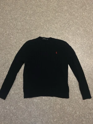 Mörkblå stickad tröja Polo Ralph Lauren - Klassisk mörkblå stickad tröja från Polo Ralph Lauren med rund halsringning och diskret röd logga broderad på bröstet. Tröjan har långa ärmar och ribbade muddar vid ärmslut och nederkant. Perfekt för lager på lager och stilren look. Köptes förra året för lite över 2000kr. Kom gärna med BUD!!