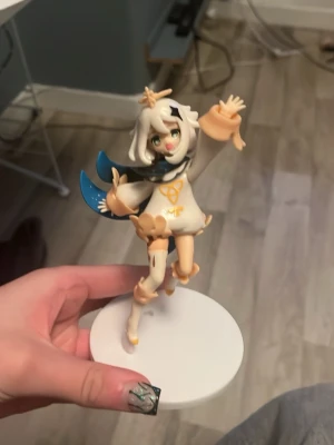 Paimon figur från Genshin Impact - Säljer en detaljerad Paimon-figur från Genshin Impact. Figuren är vit och beige med blå detaljer och står på en rund vit bas. Tillverkad i plast och perfekt för cosplay eller som samlarpryl för fans av spelet.