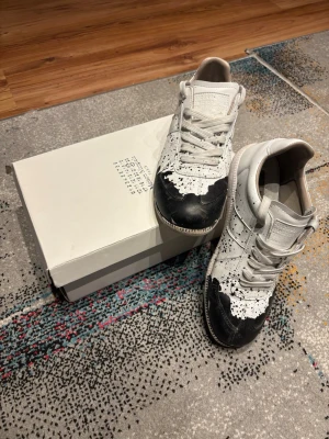 Maison Margiela sneakers svart/vit skinn - Maison Margiela sneakers i vitt skinn med svart färgstänk-design och vit snörning. Kan tänka mig och snacka pris 