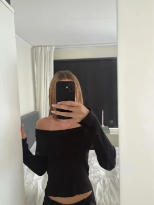 Svart off shoulder stickad tröja - Trendig svart stickad tröja med off shoulder-design och långa ärmar. Ribbstickad struktur som ger en snygg och bekväm passform. Perfekt för dig som vill ha en stilren och modern look.