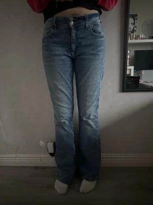 Blå bootcut jeans med broderade fickor - Säljer ett par blå jeans med bootcut passform och snygga broderade detaljer på bakfickorna. Jeansen har klassisk femficksdesign, normal midja och är gjorda i ett mjukt denimtyg. Perfekta för dig som gillar en avslappnad men ändå trendig look.