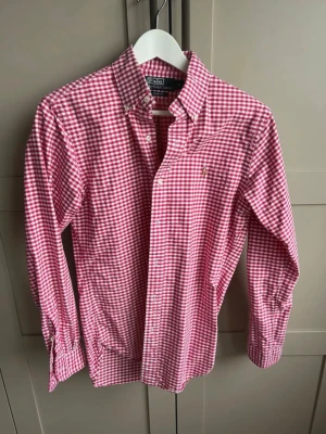 Rutig skjorta från Polo Ralph Lauren - Röd och vit rutig skjorta från Polo Ralph Lauren i slim fit-modell. Skjortan har klassisk krage, knappar framtill och lång ärm. Perfekt för dig som gillar en stilren och tidlös look.