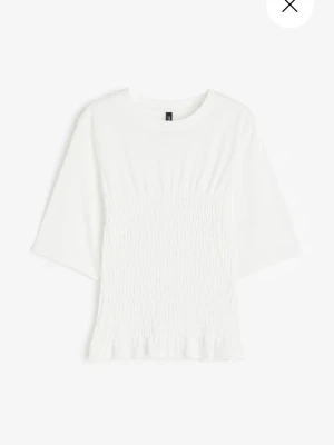 Vit topp med smock från H&M - Säljer en vit topp från H&M smockad midja och lätt volangkant nedtill. Toppen har rund halsringning. Perfekt till jeans eller kjol för en clean och fräsch look.