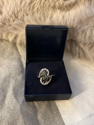 Silverring med regnbågsskimrande stenar - Unik silverring med två stora regnbågsskimrande stenar i droppform, omgivna av små gnistrande vita stenar. Ringen har en elegant och modern design som verkligen sticker ut. Perfekt för dig som gillar att synas och vill ha något extra på fingret.