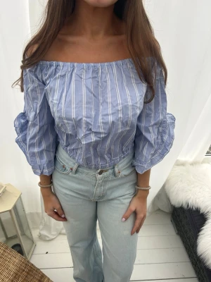 Blå offshoulder blus med puffärm - Snygg blå offshoulder blus med vita ränder och puffiga trekvartsärmar. Blusen har resår vid axlar och midja för en bekväm passform. Perfekt till jeans eller kjol💙💙Passar många storlekar🩵