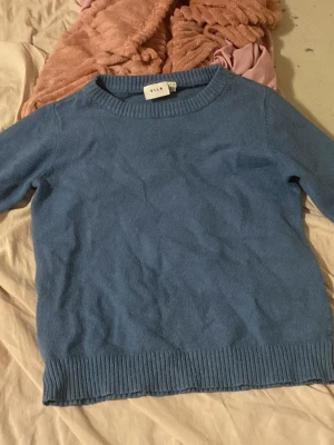 Blå stickad tröja från Vila - Mysig blå stickad tröja från Vila med rund halsringning och ribbstickade muddar vid ärmslut och nederkant. Perfekt för lager-på-lager och enkel att matcha med jeans eller kjol. Klassisk modell med lång ärm och mjukt material.