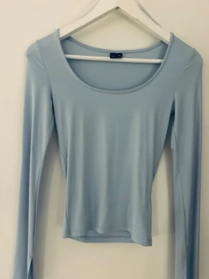 Ljusblå långärmad topp Gina Tricot - Säljer en ljusblå långärmad topp från Gina Tricot. Toppen har en rund, djup urringning och är croppad i modellen. Perfekt att styla med höga jeans eller kjol för en clean look.