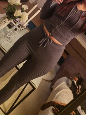 Mörkgrått ribbat loungewear-set - Säljer ett mörkgrått ribbat loungewear-set med croppad zip-hoodie och matchande höga tights. Setet har dragsko i midjan och mjukt, stretchigt material som sitter skönt på kroppen. Perfekt för chill dagar hemma eller när du vill vara bekväm men ändå snygg.