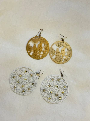 Två par runda statementörhängen - Två par stora runda örhängen. Ett par i guld med utskurna fåglar och blommor, och ett par i silver med blommönster och små glittriga stenar. Båda paren är lätta och har krokar för enkel användning.