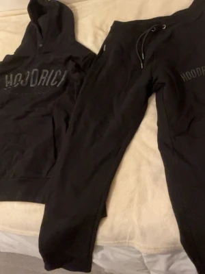 Svarta Dress från Hoodrich - Svarta mjukisbyxor från Hoodrich med dragsko i midjan och diskret logga på benet. Sköna och stilrena byxor i mjukt material, perfekta för chill eller streetwear. Matcha med hoodie för en komplett look.