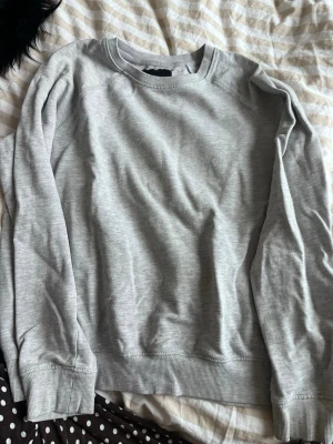 Grå sweatshirt från 157 - En basic grå sweatshirt från 157 med rund halsringning och ribbade muddar vid ärmslut och nederkant. Tillverkad i mjukt material som känns skönt mot huden. Perfekt för en avslappnad och stilren look.