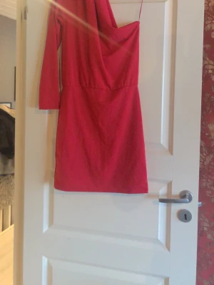 Röd asymmetrisk klänning Bik Bok - Snygg röd klänning från Bik Bok med asymmetrisk design, en lång ärm och en axelbandsdetalj. Klänningen har en kroppsnära passform och är gjord i ett mjukt, stretchigt tyg som ger en skön känsla. Perfekt för dig som vill sticka ut.