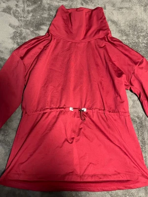 Röd polotopp med snörning i midjan - Snygg röd polotopp med lång ärm och justerbar snörning i midjan för en cool siluett. Tillverkad i mjukt bomullsmaterial som känns skönt mot huden. Perfekt för dig som gillar en enkel men ändå unik look. 