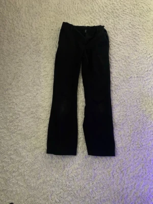 Svarta kostymbyxor från Lindex Kids - Stilrena svarta kostymbyxor från Lindex Kids i storlek 140. Klassisk rak passform med hällor för bälte och diskret dragkedja framtill. Perfekta för en dressad look och tillverkade i mjukt material för skön känsla.