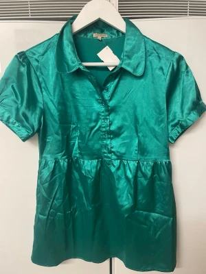 Grön söt gullig blus bik bok - Supersöt härlig grön satinliknande blus. Passar både till jeans och ett par snygga pumps eller kängor eller varförutan inte kostymbyxor och stövletter? Piffar upp hela din outfit på ett elegant och trendigt sätt. Du kommer göra succé!