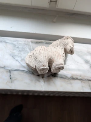 Handgjord häst i lera - En unik, handgjord hästfigur i ljus lera med tydliga räfflor och detaljerad man. Perfekt som dekoration eller personlig prydnad. Figurinens form är robust och stiliserad, vilket ger den en charmig och rustik känsla.