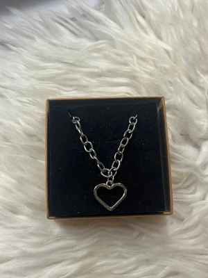 Chunky silverfärgat halsband med hjärta - Stilrent halsband med grov kedja i silverfärgad metall och ett öppet hjärthänge. Perfekt accessoar för att ge din outfit en edgy och trendig touch. Levereras i ask.