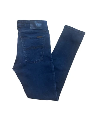 Mörkblå Nudie Jeans  - Snygga mörkblå jeans från Nudie Jeans med klassisk femficksdesign och diskret logga på bakfickan. Jeansen har en smal passform och är tillverkade i mjukt denimtyg av bomull med stretch för extra komfort.