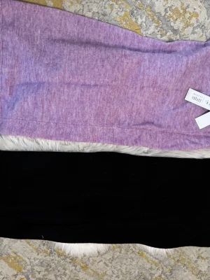 Lila och svart kjol i mjukt tyg - Två raka kjolar i lila och svart, båda i mjukt och stretchigt material. Den lila kjolen har en melerad look och båda har enkel, minimalistisk design utan synliga detaljer. Perfekta att matcha med en crop top eller hoodie.